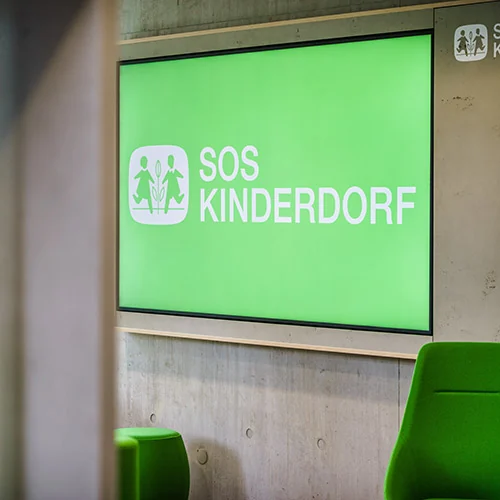 Beleuchtete Wandfläche mit SOS-Kinderdorf Logo im Innenraum der Botschaft für Kinder