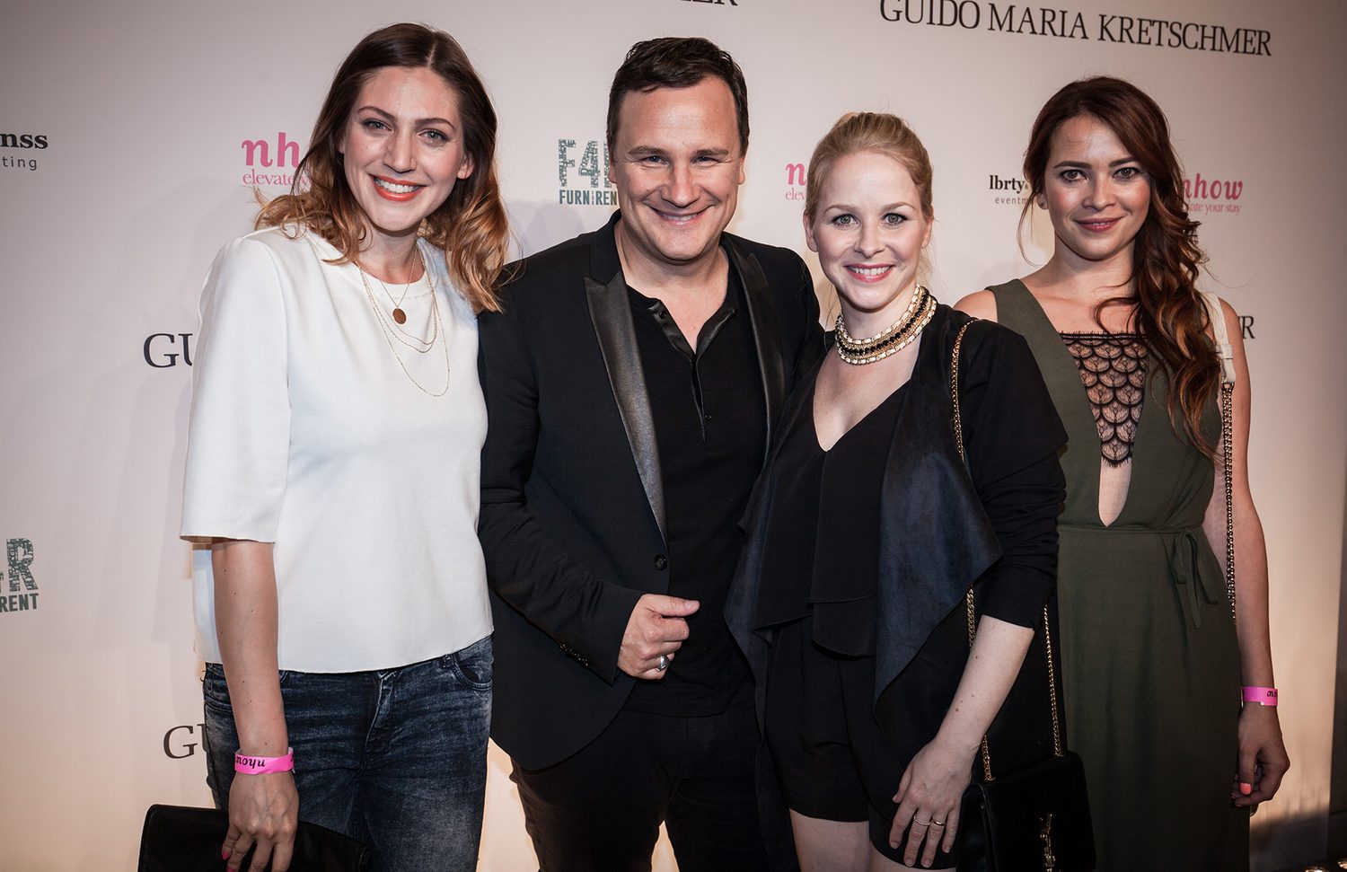 Guido Maria Kretschmer mit drei Gästen vor der gebrandeten Pressewand der Aftershow-Party in Berlin